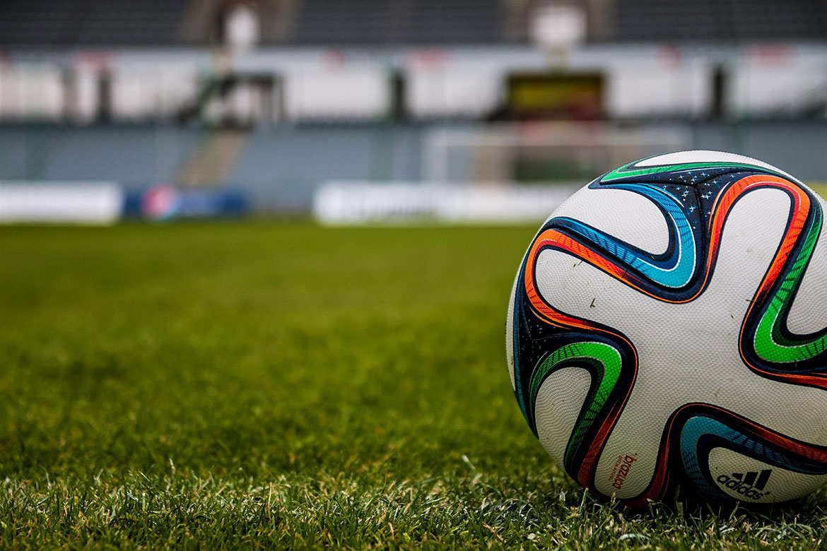 Fußball auf grünem Rasen in einem leeren Stadion, im Hintergrund verschwommene Tribünen.